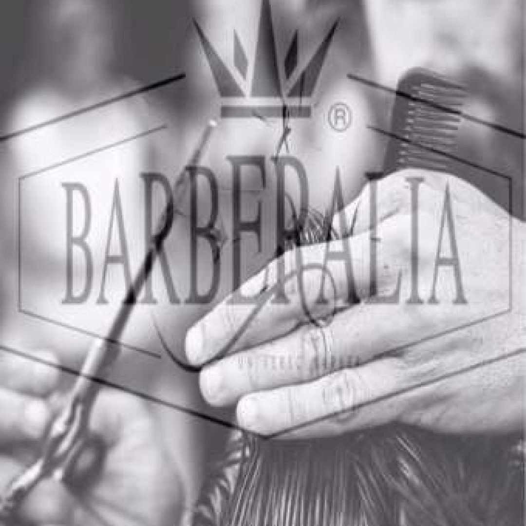 Fotografía en blanco y negro de manos de un barbero cortando el cabello con tijeras y peine, con el logotipo "BARBERALIA" superpuesto en el centro.